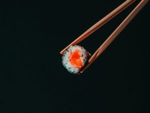 Salmon sushi roll hold with chopsticks on black background