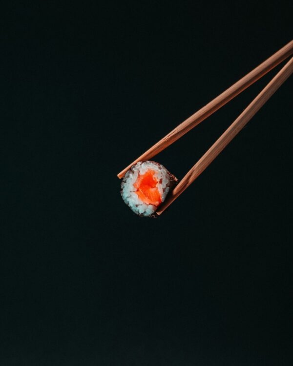 Salmon sushi roll hold with chopsticks on black background